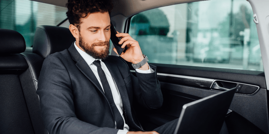 A man in a suit and tie sits in a car's back seat, engaged in a phone conversation.